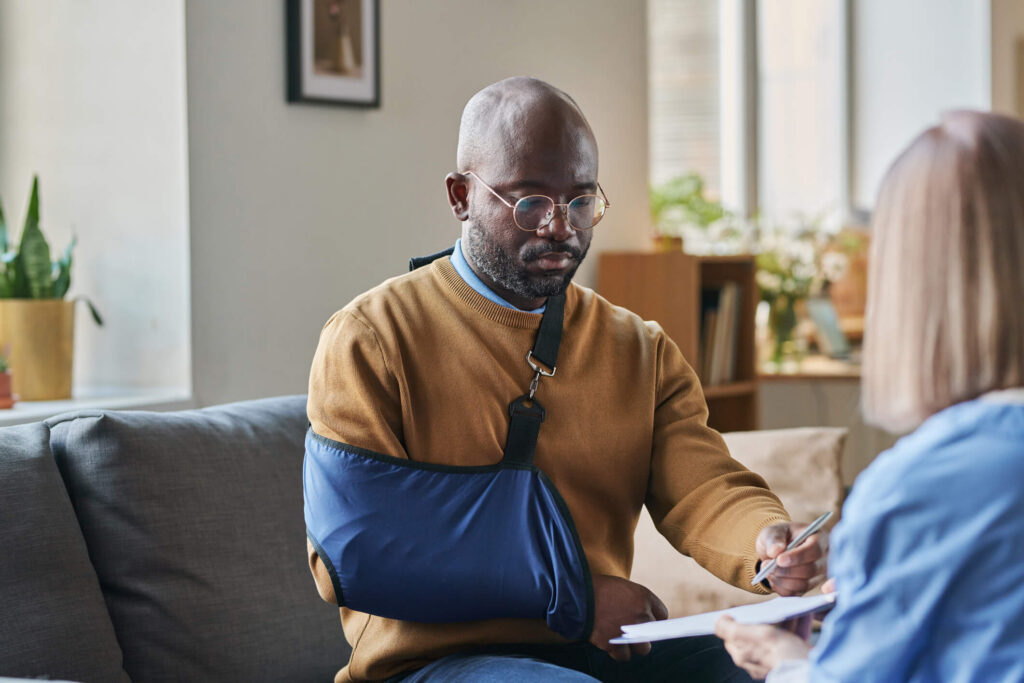 black man with arm in sling, signing paperwork