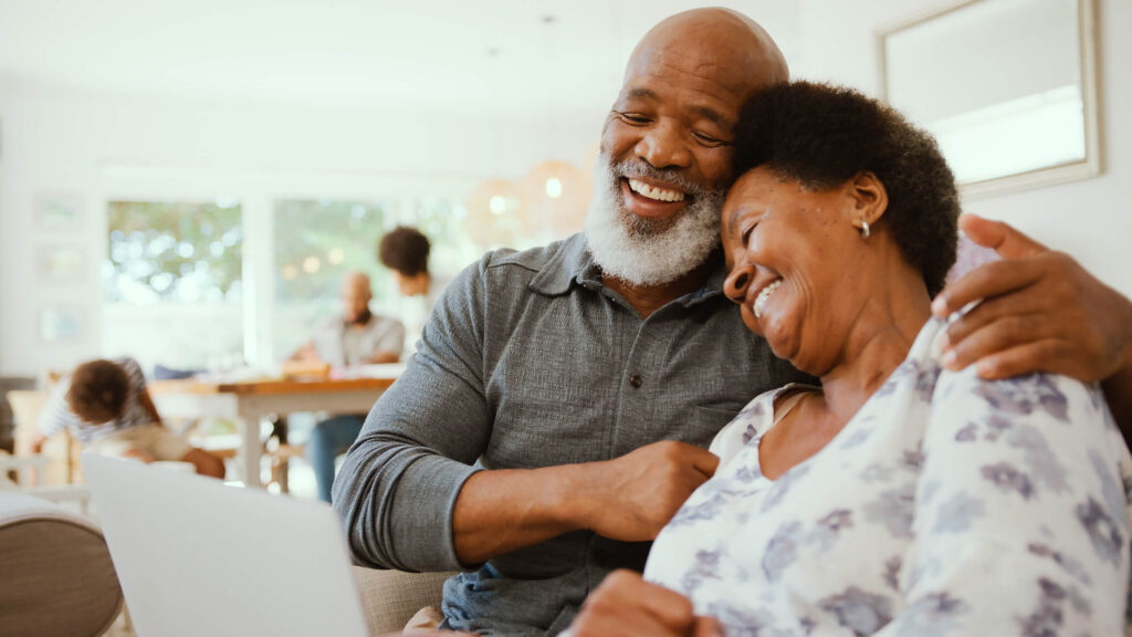 older black couple hugging on the couch, enjoying family in the background